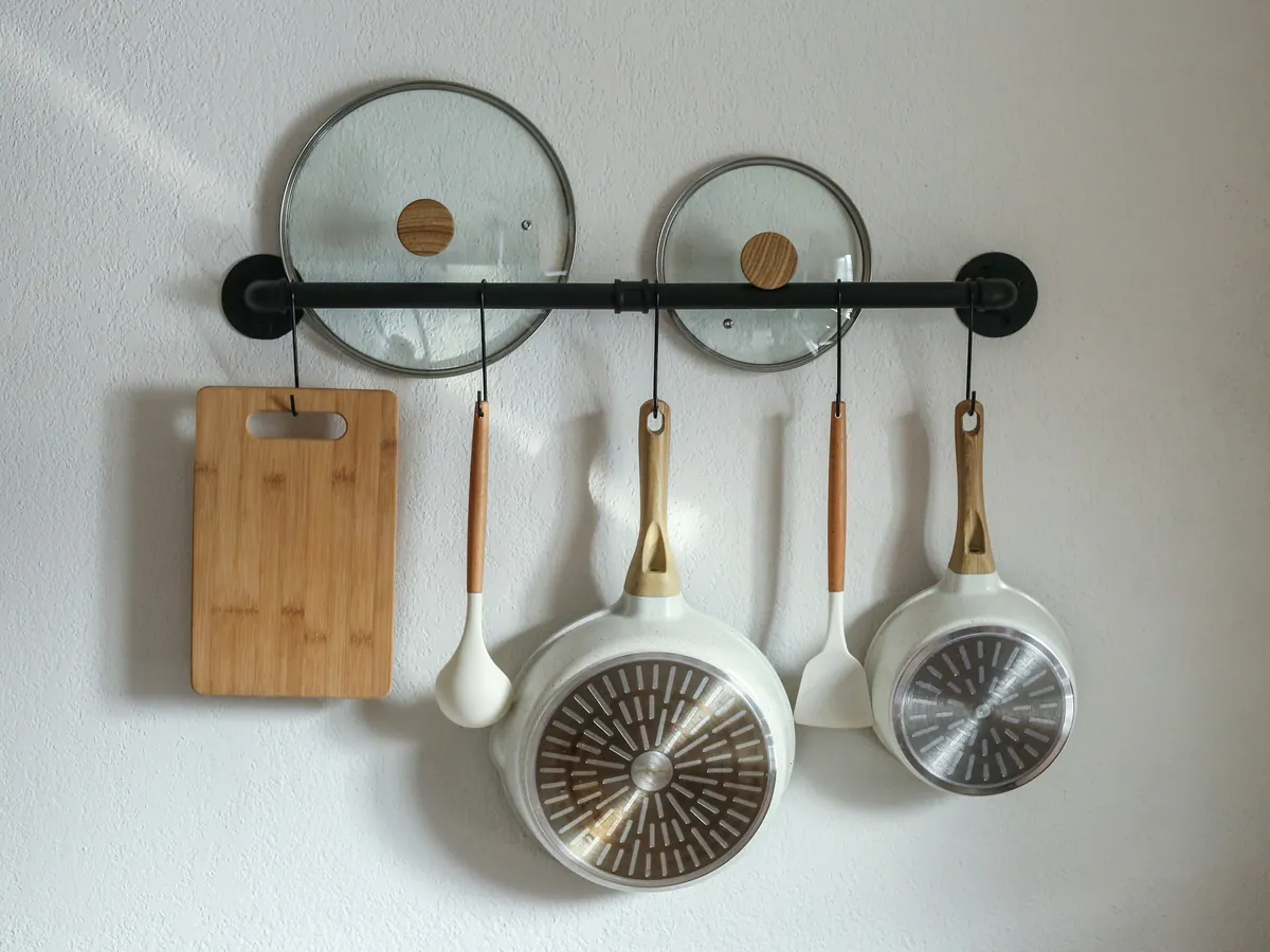 Pans, lids, a cutting board and utensils on a wall rail