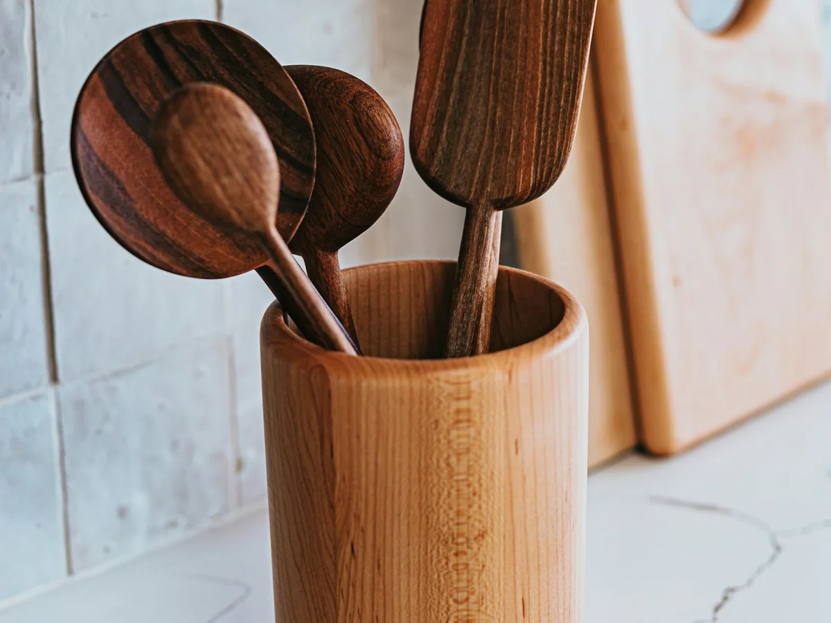 Wooden spoons and spatula in a wooden holder, with cutting boards behind